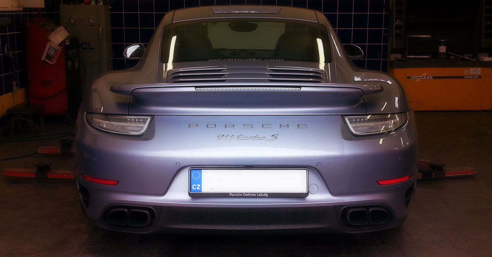 stříbrné Porsche 911 Turbo S uvnitř dílny, pohled zezadu